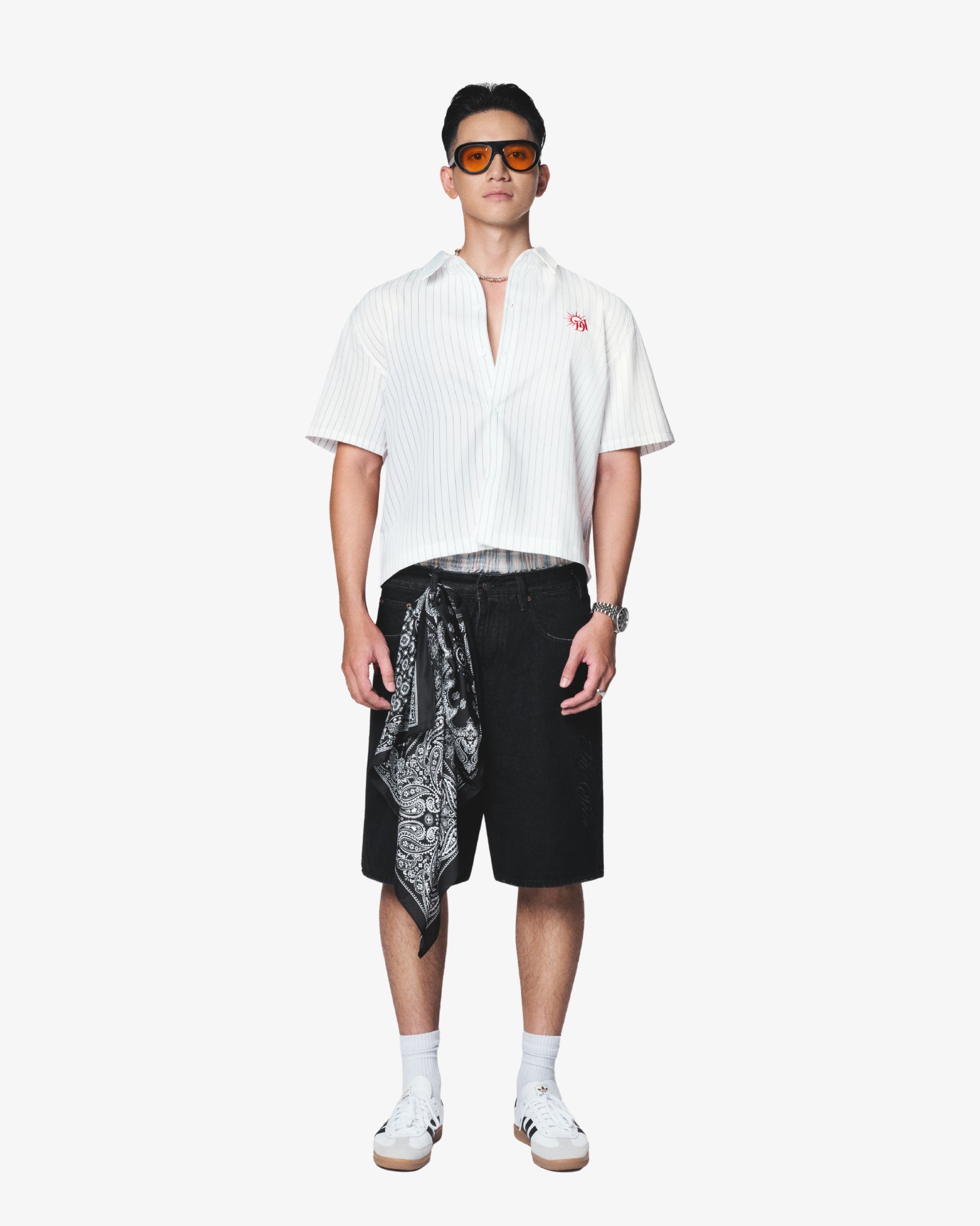 Man wearing a white shirt, black shorts with a pattern, and sunglasses on a white background