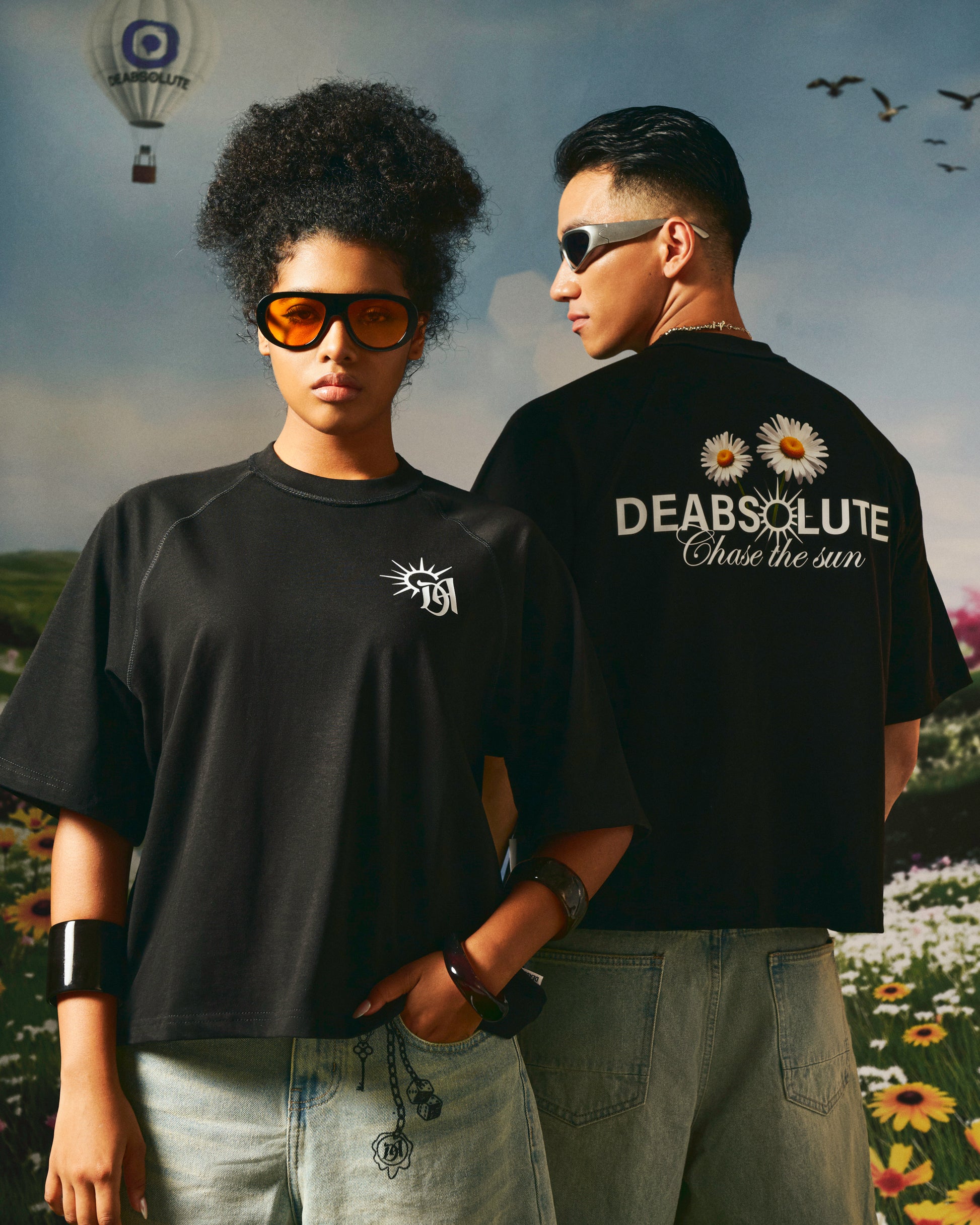 Two people wearing black t-shirts with visible branding against a scenic background.