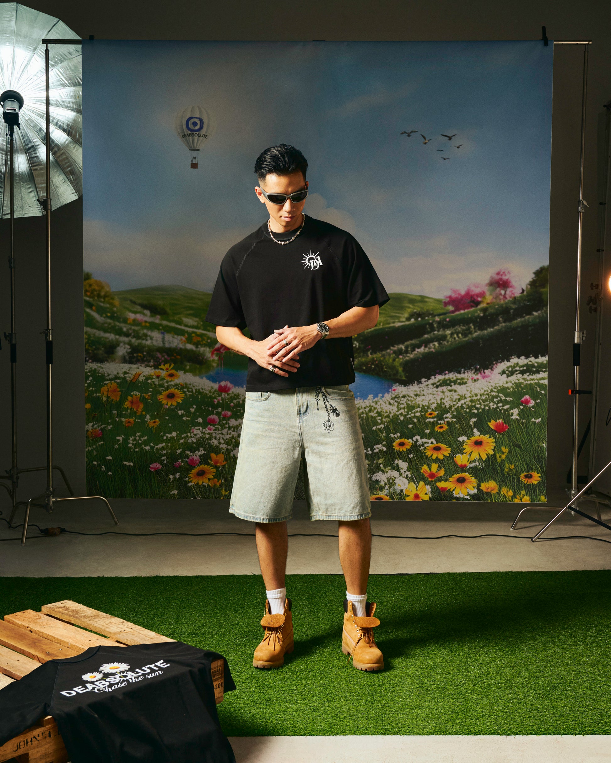 Person wearing a black t-shirt with a logo, standing in front of a scenic backdrop with flowers and trees.