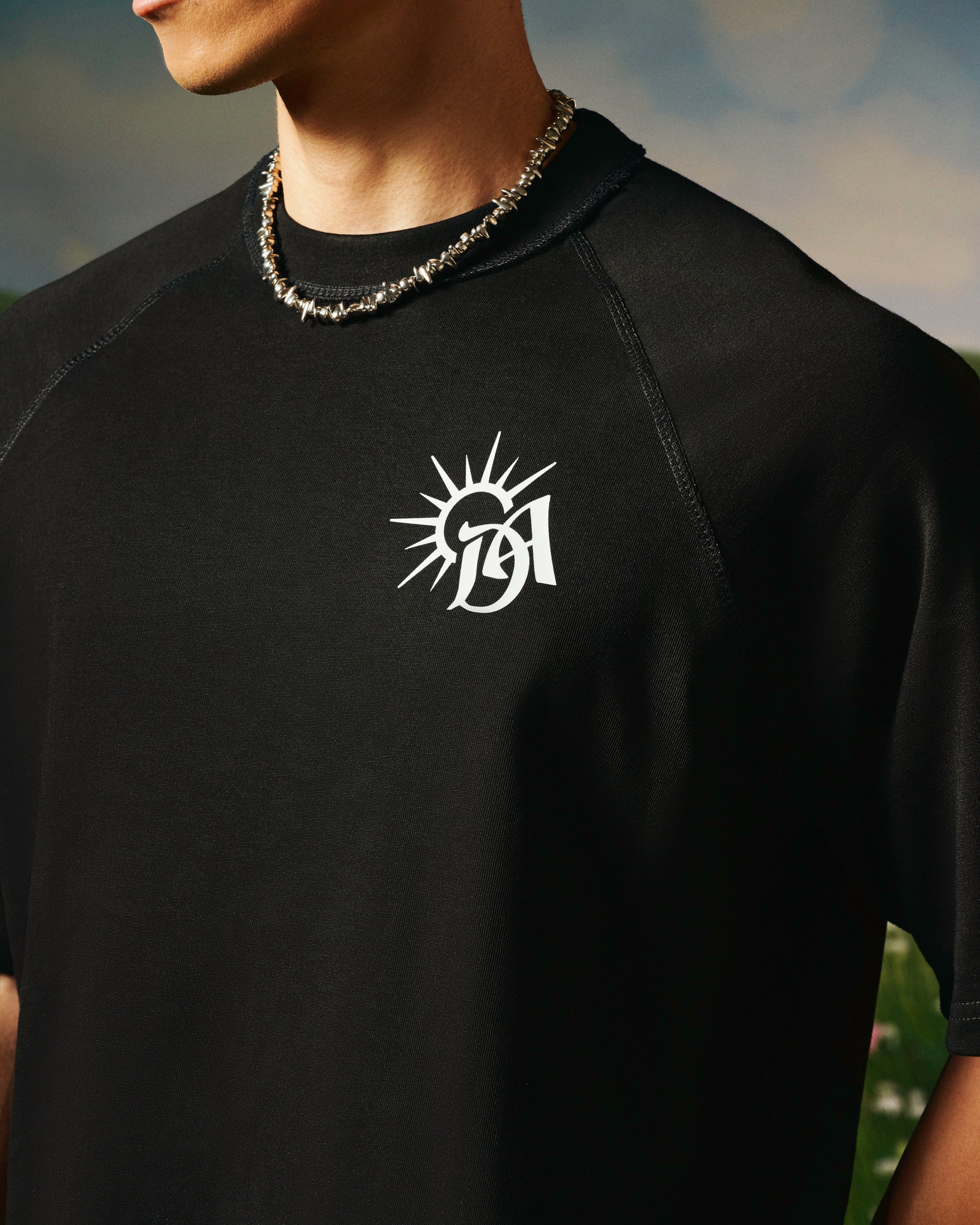 Black t-shirt with a white logo on a person wearing a chain necklace.