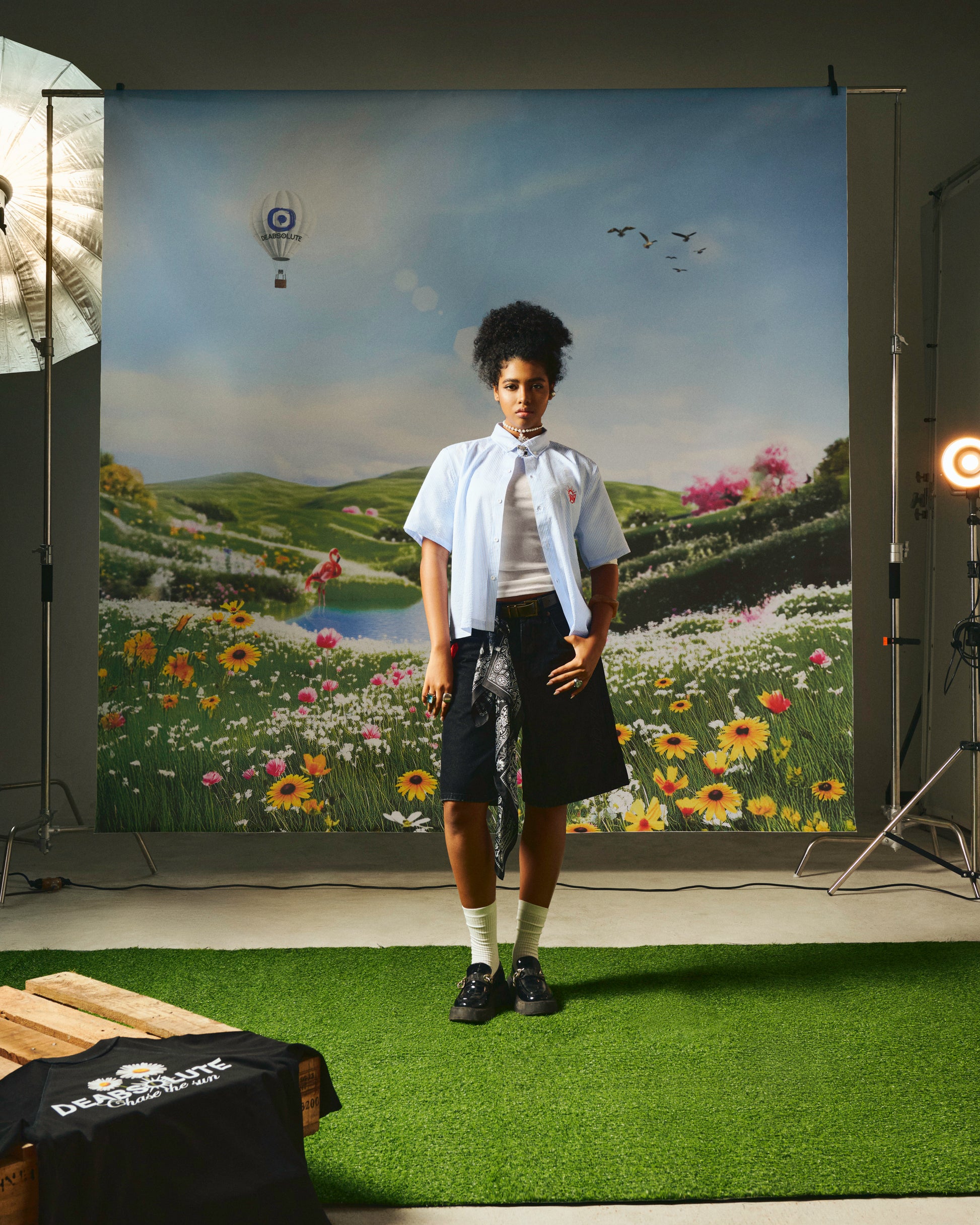 Person standing in front of a scenic backdrop with grass, flowers, and a lake.