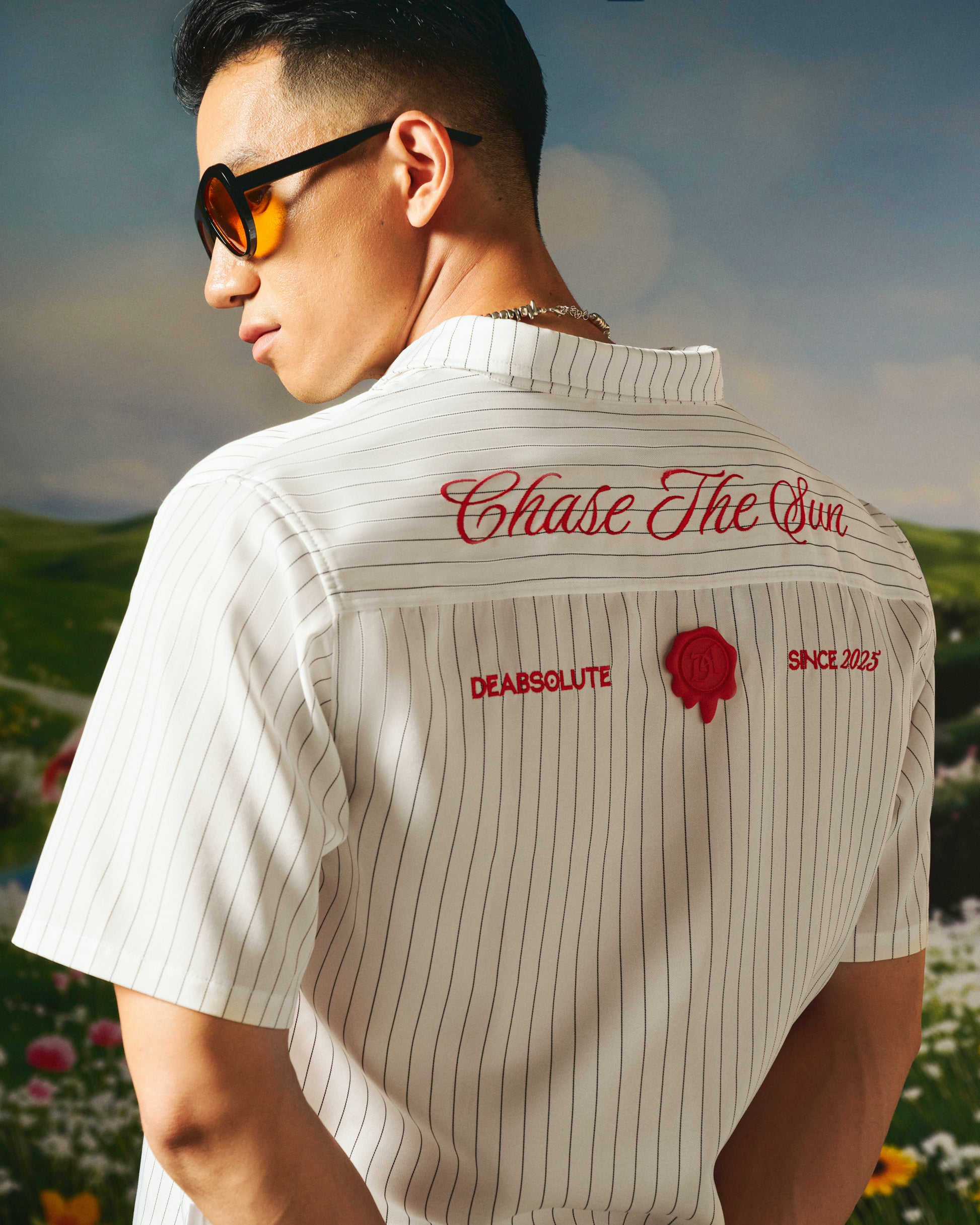 Man wearing a white striped shirt with text and logos, standing outdoors.