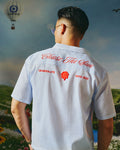 Person wearing a white shirt with text and logos, standing against a scenic background with hot air balloons.